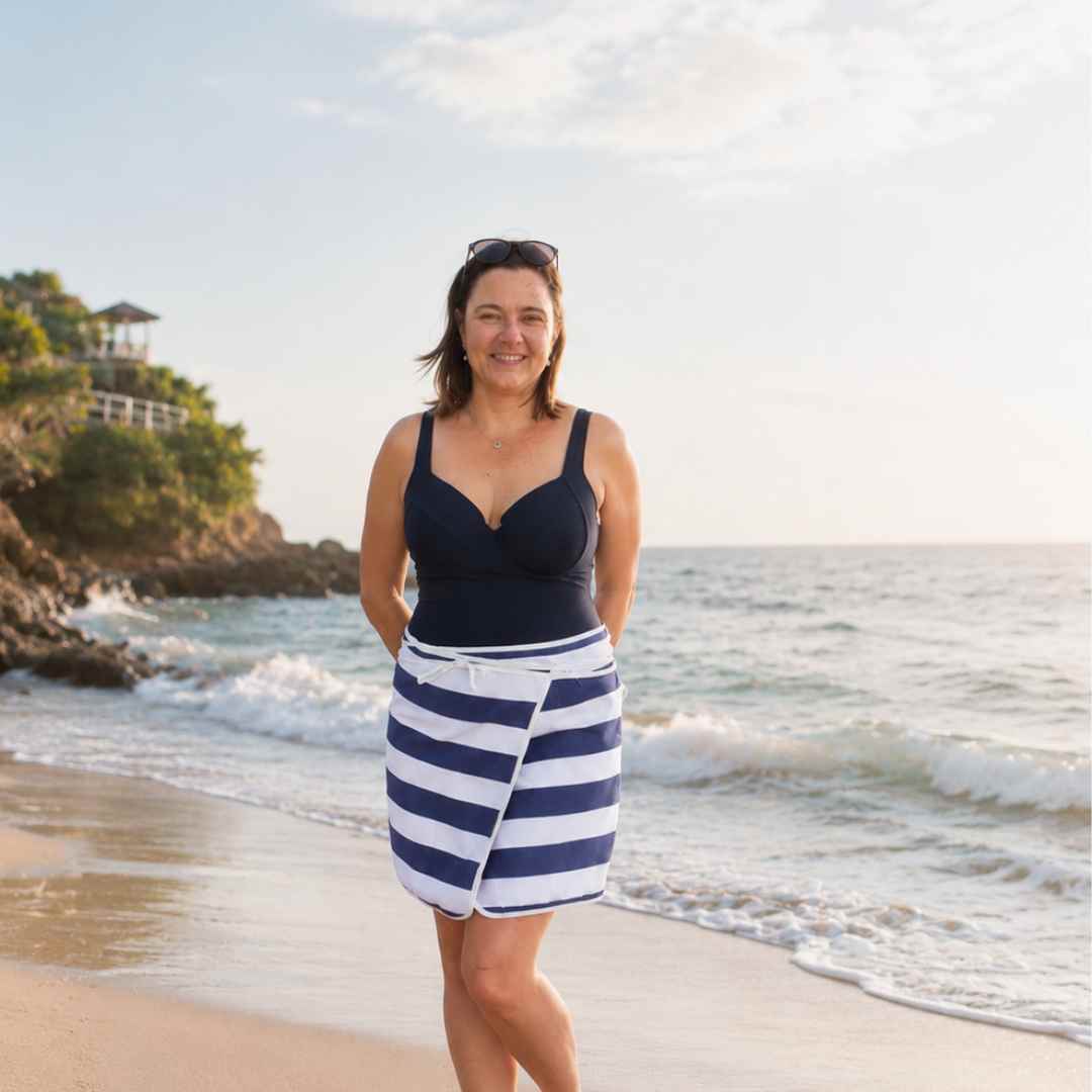 Woman standing on a beach wearing a navy blue top and white striped towel wrap beach skirt.