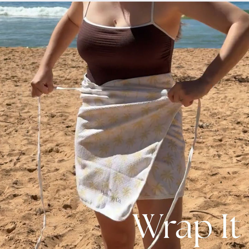 Person on a beach holding a white towel with yellow patterns, with 'Wrap It' branding.
