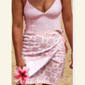 Person wearing a pink patterned sarong holding a pink flower on a beige background