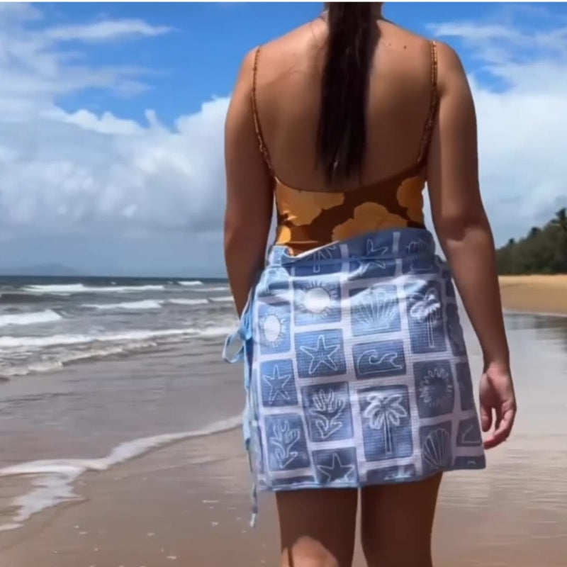 Person on a beach wearing a patterned top and blue skirt with starfish design.