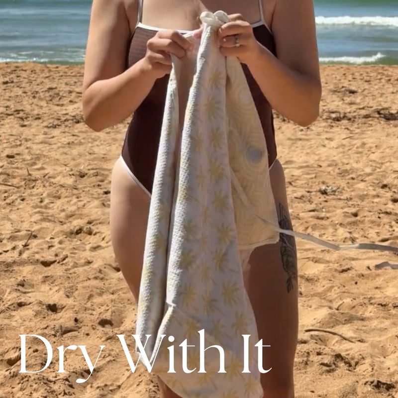Person holding a towel with a beach background and 'Dry With It' text.
