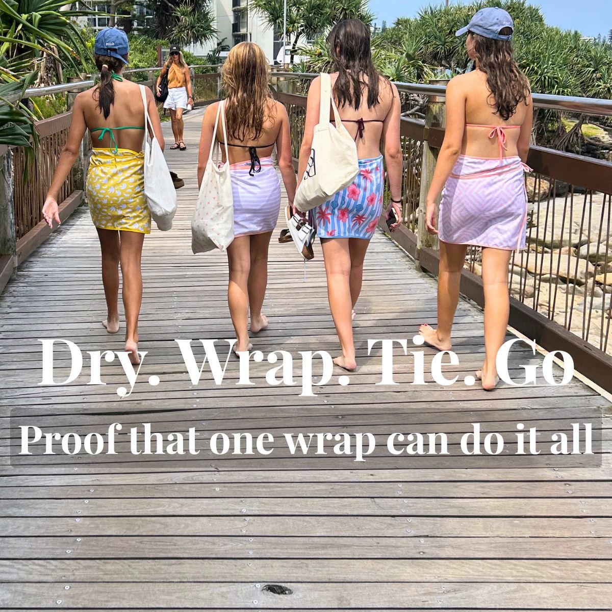 Four women walking away on a wooden boardwalk wearing colorful reusable towel wraps around their midsections. Large text overlay reads 'Dry.