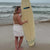 girl holding surfboards waling on sand