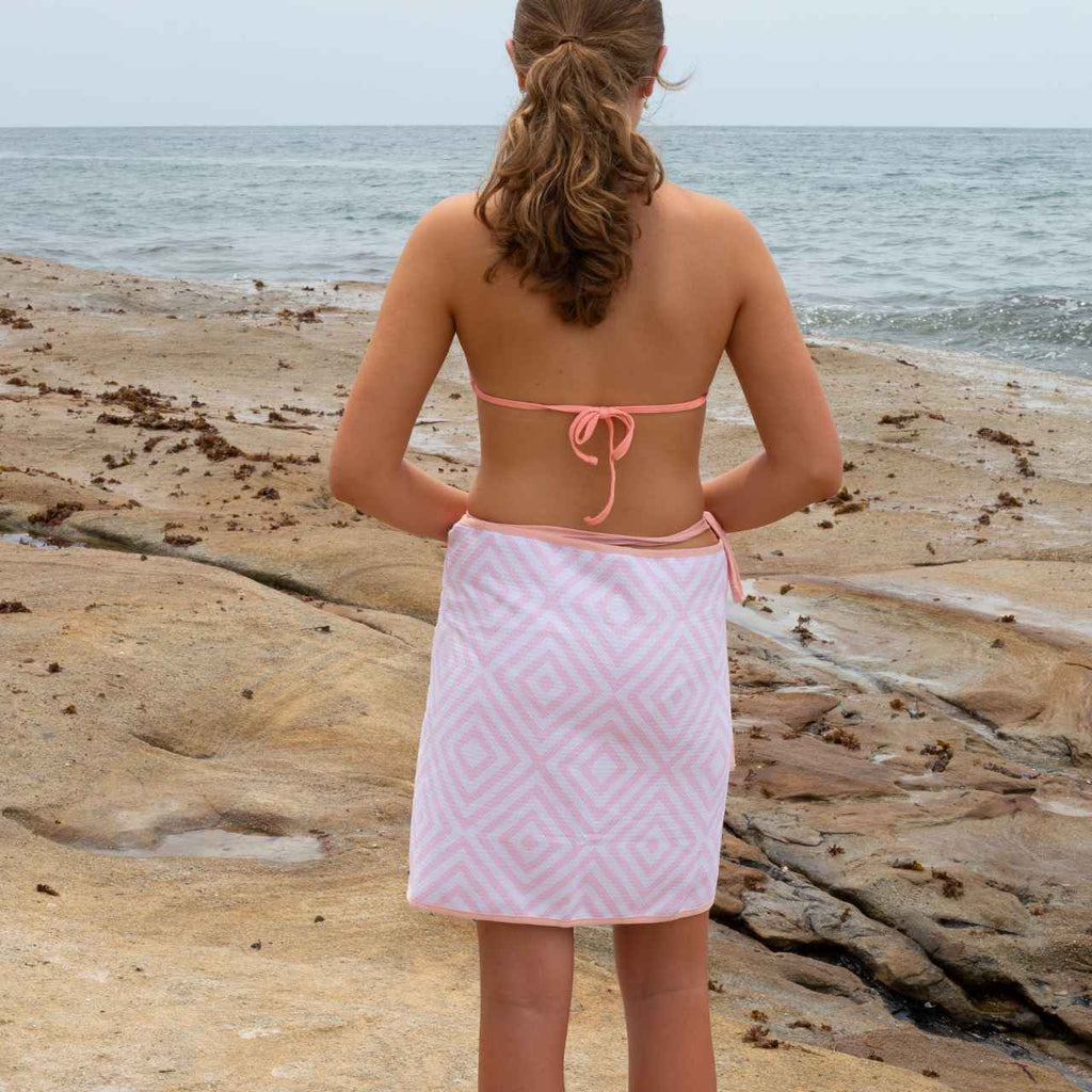 Person wearing a pink diamond patterned towel on a beach