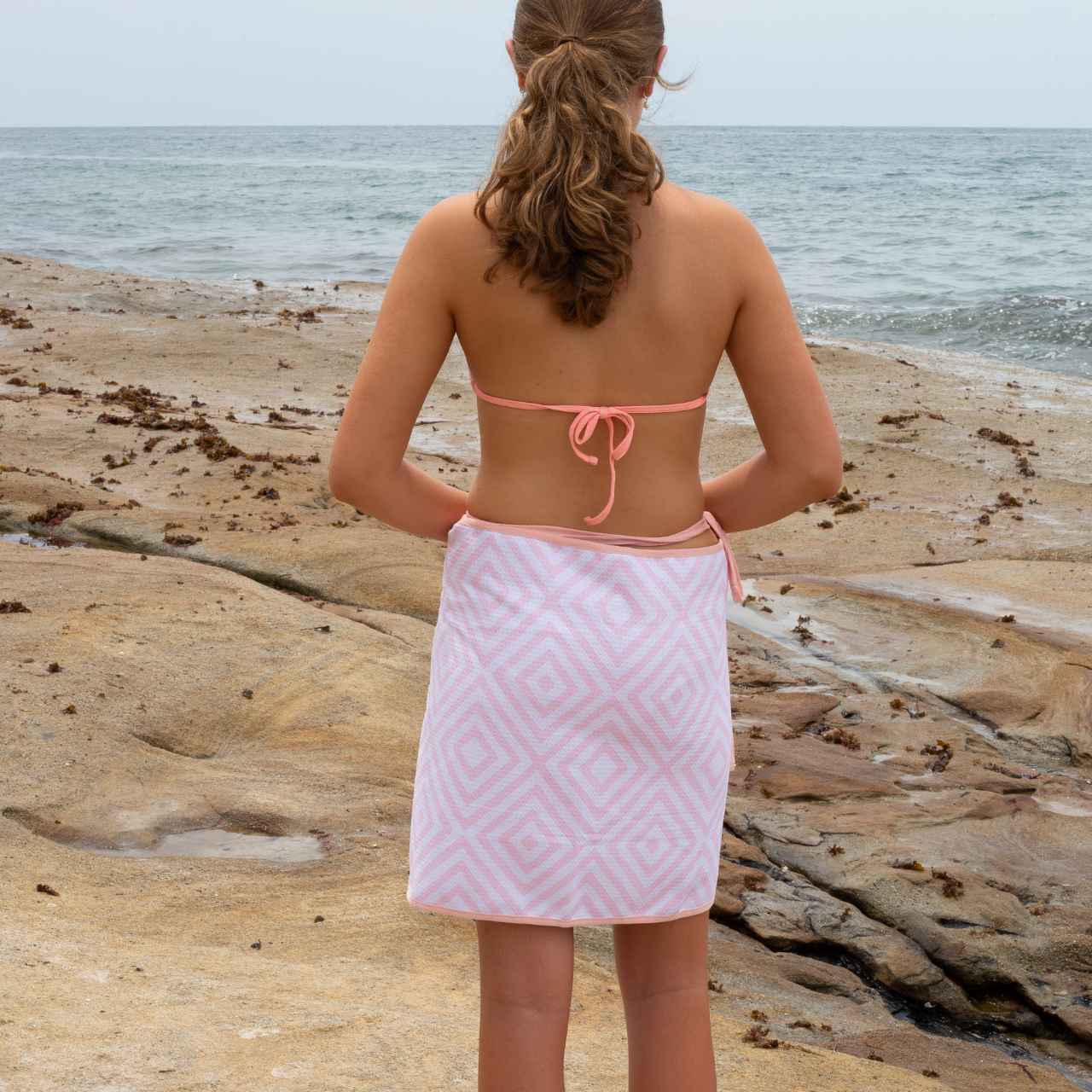 Person wearing a pink diamond patterned towel on a beach