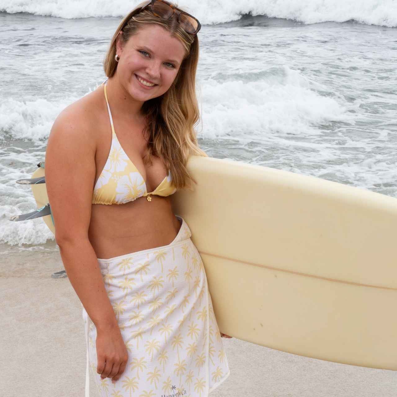 Woman holding a surfboard on a beach with ocean waves in the background